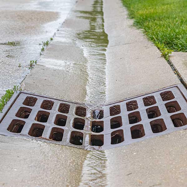 Closeup of rain water running down street gutter and flowing into storm sewer system drainage grate
